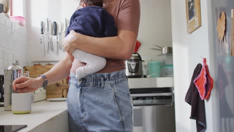 video de una madre caucásica sosteniendo a un recién nacido y preparando té