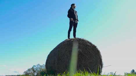 man standing on a hay bale in a field