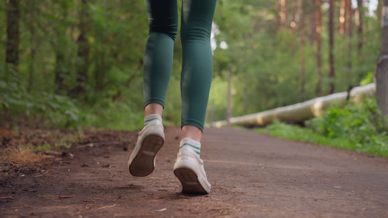 corredora femenina corriendo por el camino en el parque. piernas de mujer en zapatos deportivos corriendo por un camino rodeado de árboles. mujer entrenando en la naturaleza en un día de verano