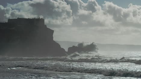 Waves-crash-on-the-rock-with-the-Farol-da-Nazaré-fortress-Beautiful-cinematic-slow-motion-shot