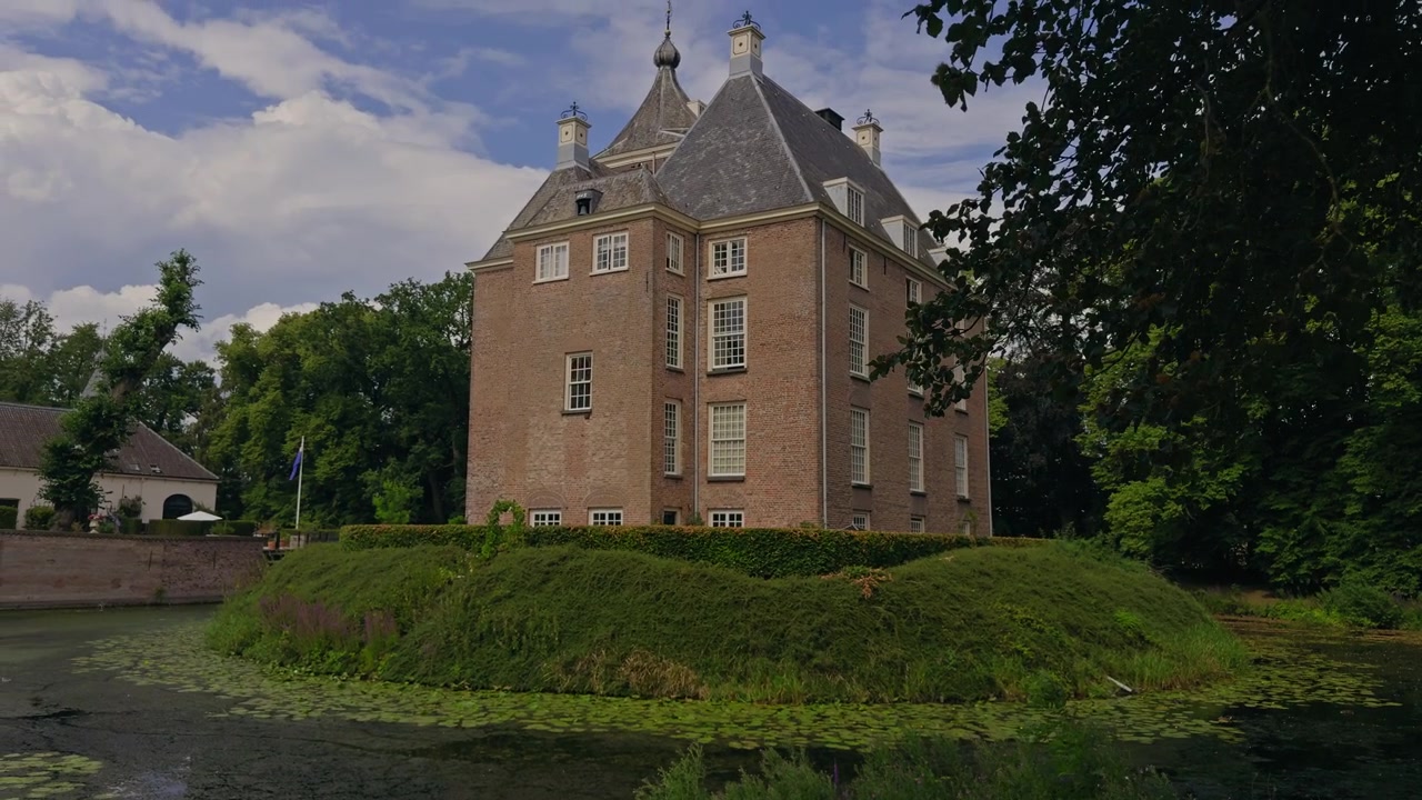 Castello di Neerijnen in Olanda, circondato dal suo fossato storico e dalla vegetazione lussureggiante sotto un limpido cielo estivo blu
