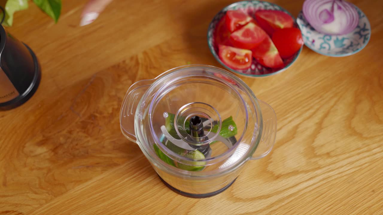 Cooking preparation, putting cucumber into small food processor. Closeup