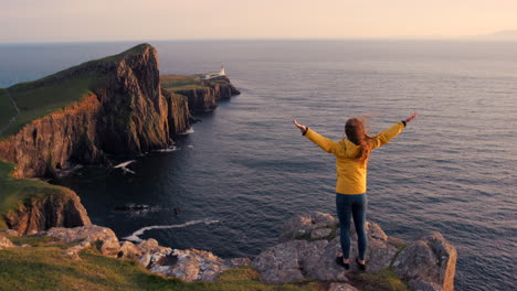 woman celebrating scenic view of scottish lighthouse at sunset