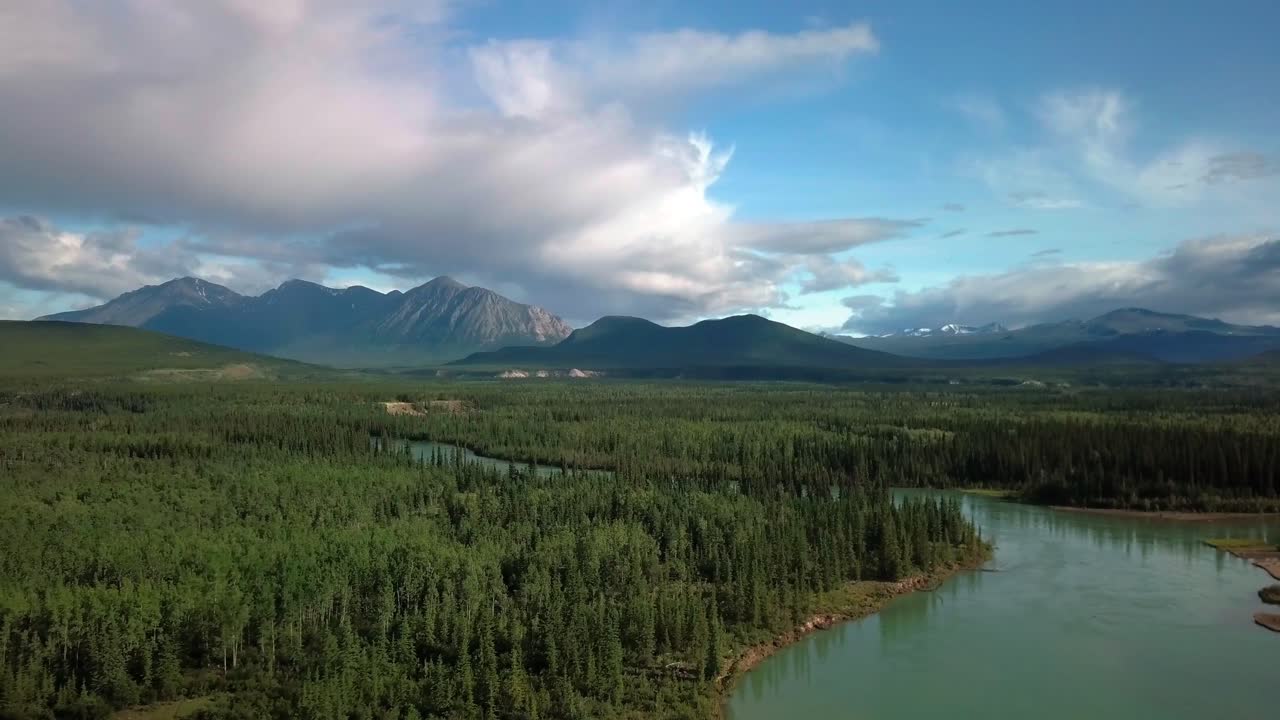 Impressive and grand scene of Yukon landscape above teal Takhini river, evergreen forest and green vegetation in Ibex valley towards Mount Ingram on dramatic blue sunny sky day, Canada, drone approach