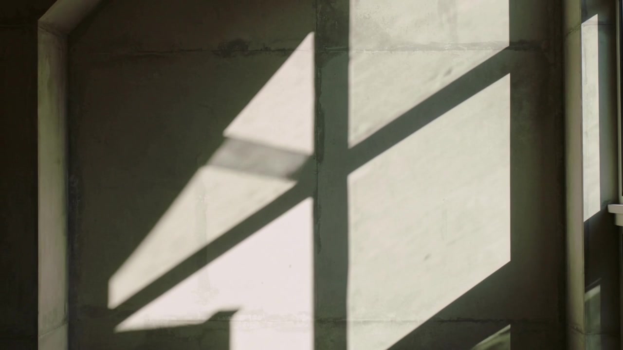 Luz solar que se move projetando sombras de janela em uma parede de concreto interior, formando um lobo diagonal e recortes.
