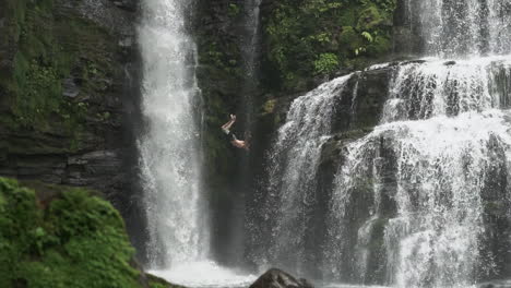 shot following man as he does backflip off jungle waterfall, slow motion