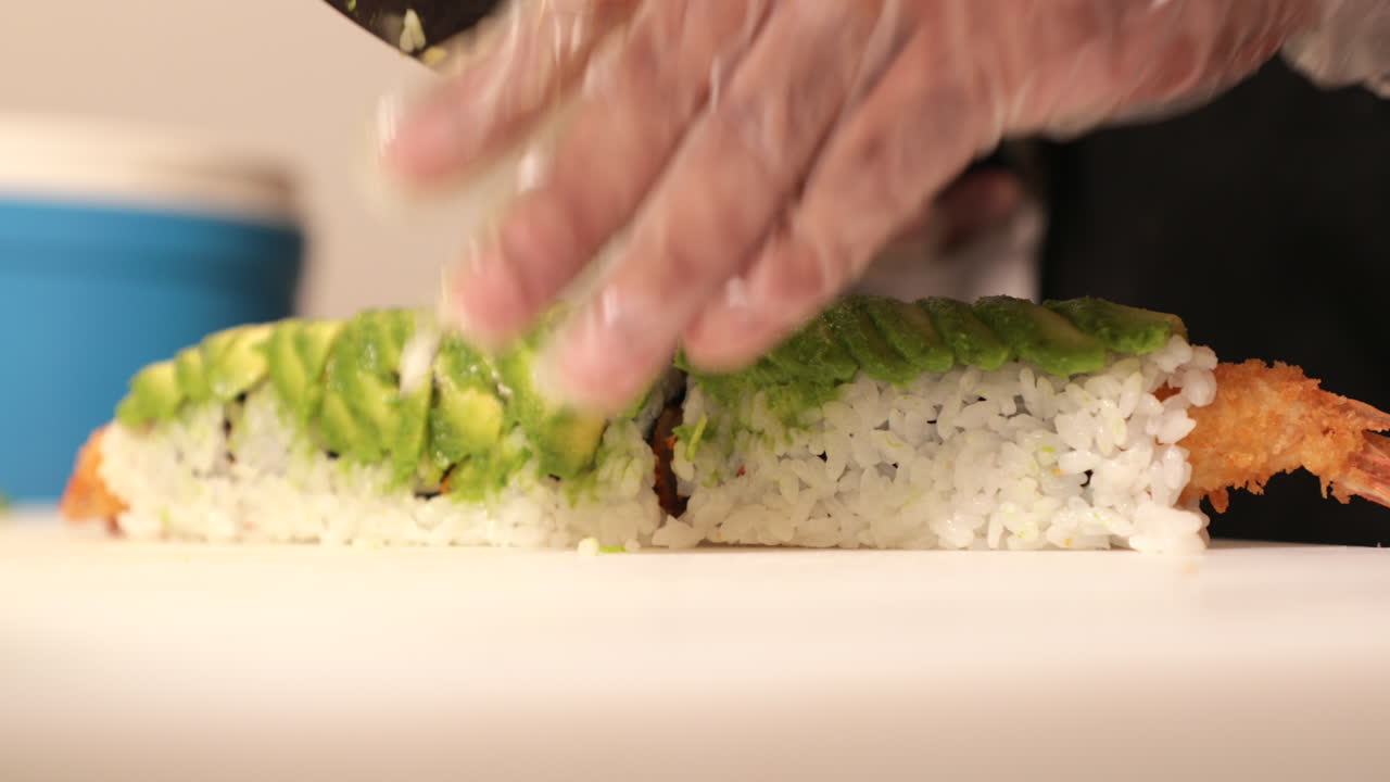 chef cortando los rollos de sushi con camarones tempura fritos y aguacate verde