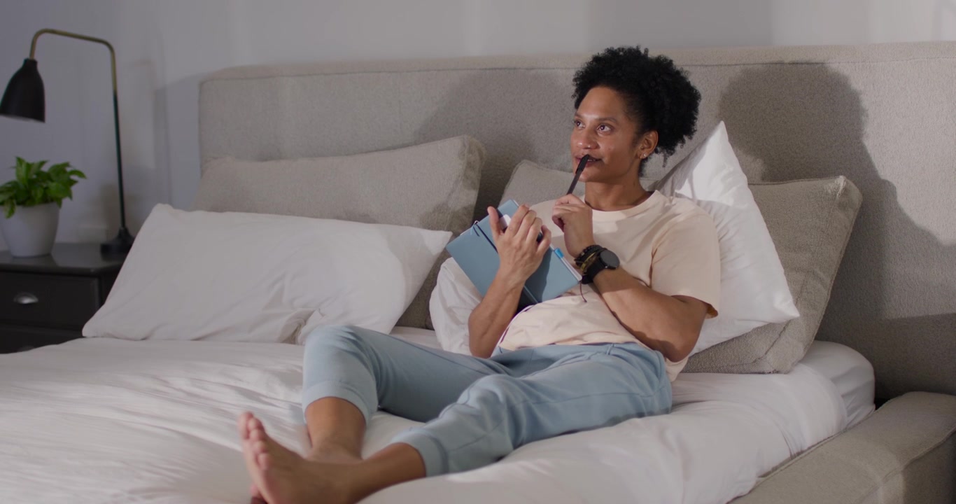 Uomo afroamericano seduto sul letto, che solleva un tablet blu, usando uno stilo e controllando i contenuti.
