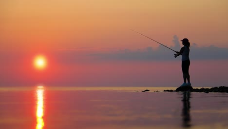 frau fischt auf einer angelstange, die sich im hintergrund beim sonnenuntergang dreht.