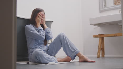 disappointed woman sitting on bathroom floor at home with negative home pregnancy test