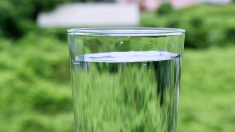 vaso de agua con gotas que caen en llenarlo con cada gota mientras que el fondo es verde también se refleja significando el valor del agua