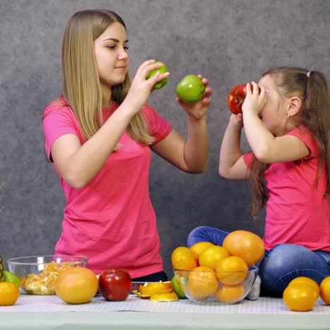 mother and daughter playing with fresh fruit. little girl and a woman in pink t-shirts spending time together in the kitchen. organic fruits on the table.