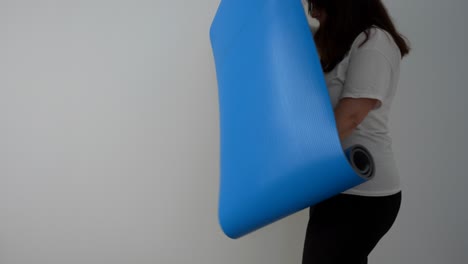 pregnant woman unrolling a blue exercise mat. static indoor
