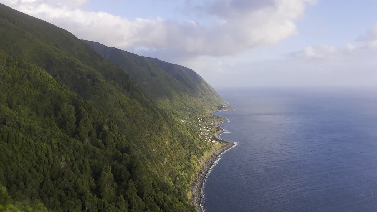 mujer turista china malaya asiática tomando fotos de los espectaculares acantilados sobre el océano atlántico con un pueblo rural, un exuberante paisaje verde, la isla de são jorge, las azores, portugal