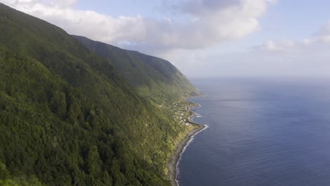 Asian-Malaysian-Chinese-Tourist-Woman-taking-photos-of-the-dramatic-cliffs-over-the-Atlantic-ocean-with-a-rural-village,-lush-green-landscape,-São-Jorge-island,-the-Azores,-Portugal