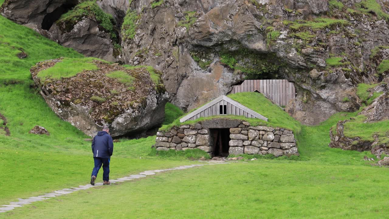 Mies kävelee kohti kivimökkiä Islannissa 4K.