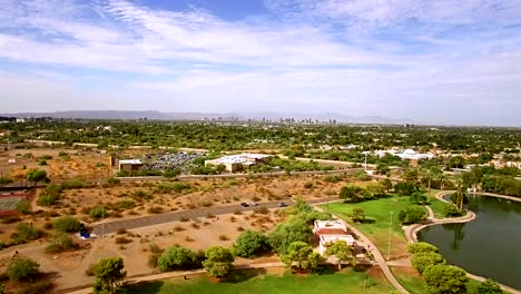 Aerial-pull-back-from-a-desert-parking-lot-and-the-city-of-Phoenix,-Arizona-skyline-to-reveal-Granda-city-park-complete-with-water-feature