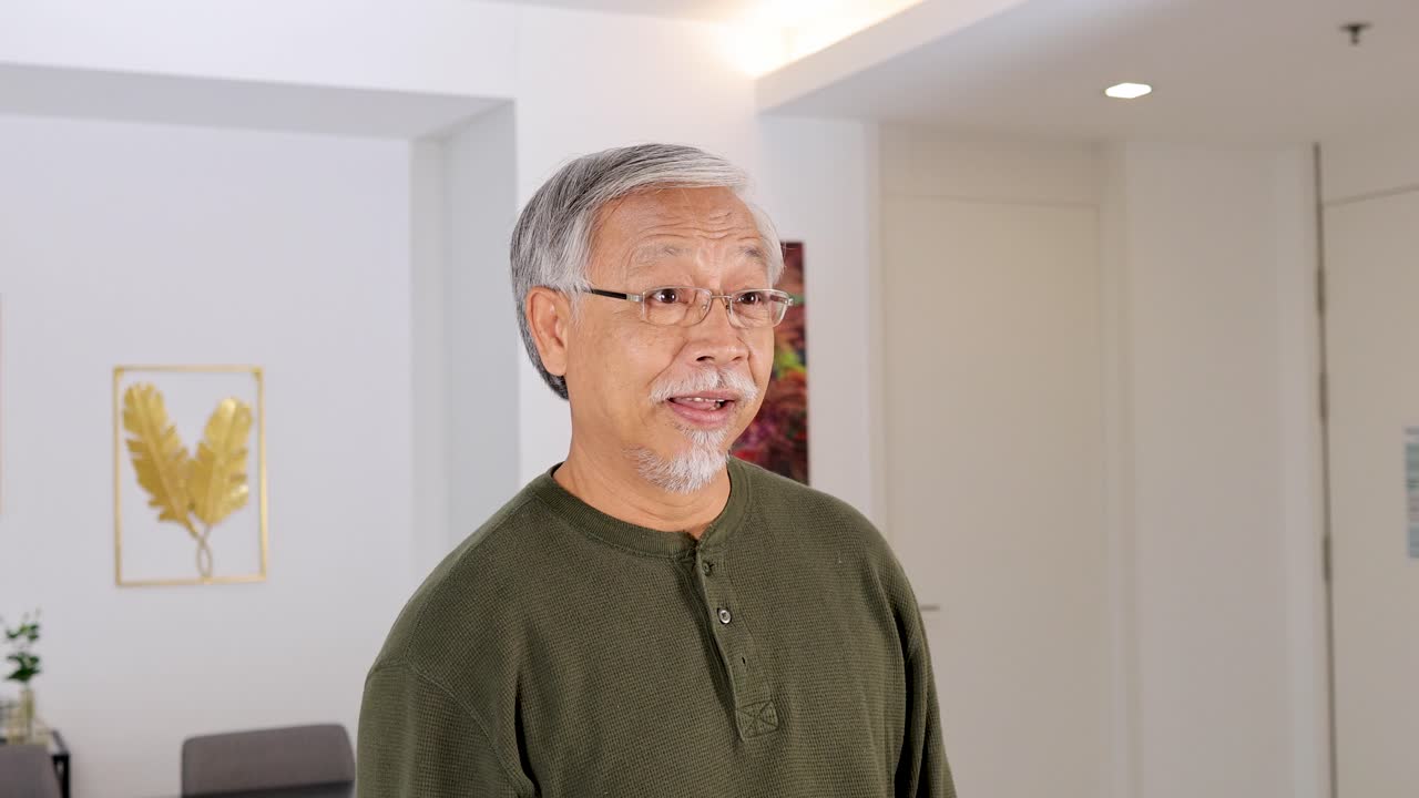 Senior man mimics phone call gesture, smiling, in bright modern living room, static camera