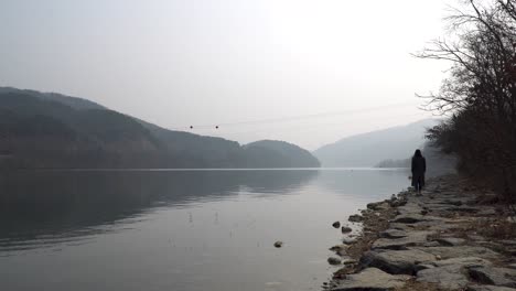 Nami-Island,-a-woman-walking-on-the-bank-of-North-Han-river-in-a-misterious-way