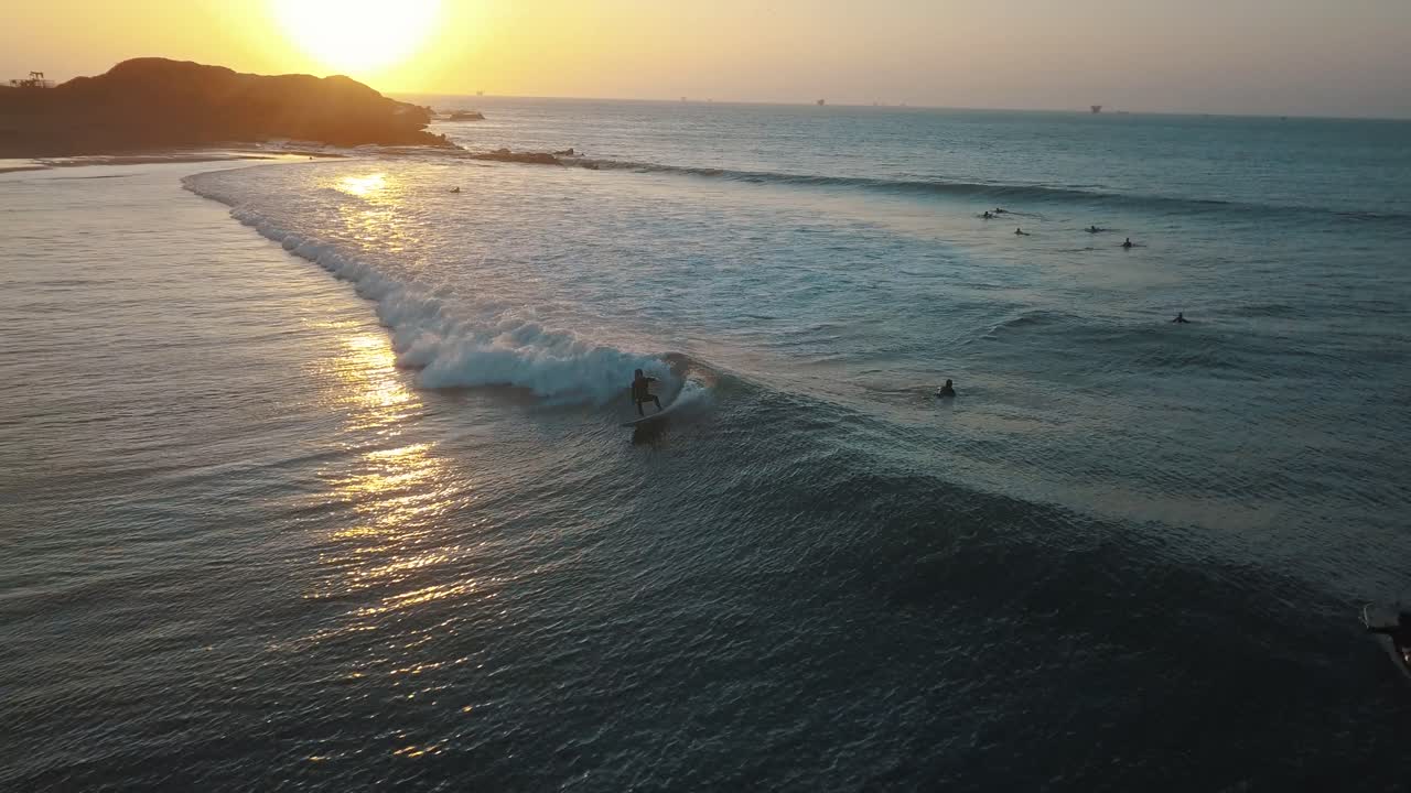 Drone Aerial view following a pro surfer, during sunset, at the coast of Talara, in Peru - tracking, drone shot