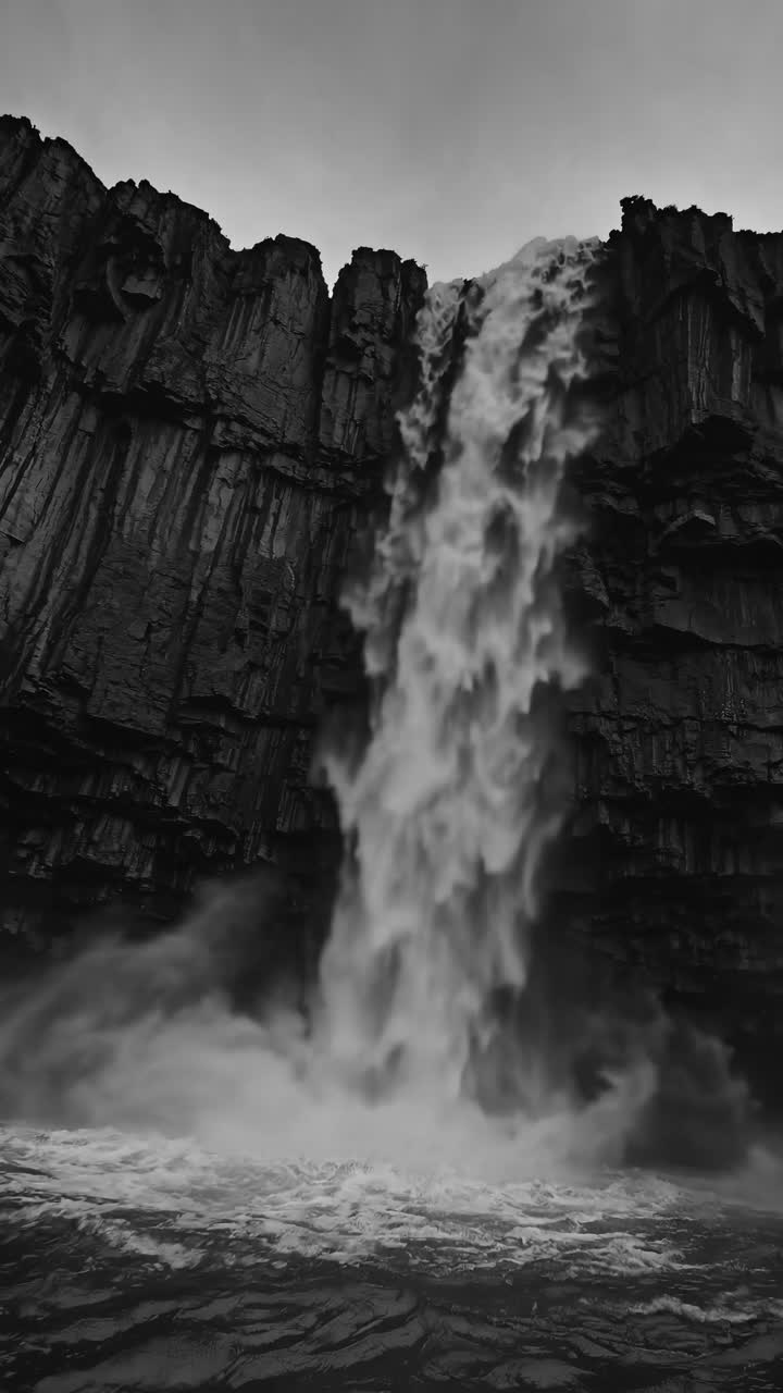 Dramatic black and white video of a waterfall cascading down rugged cliffs, captured from a low