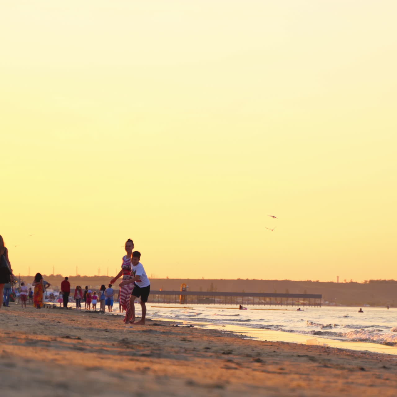 Joyful woman with a boy spending a good time at seaside. Happy mother is running together with her son on the seashore in the evening. Summer vacation.