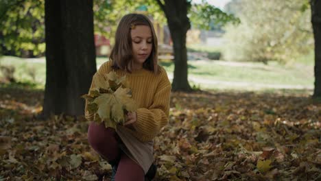 little girl looking for leaves in public park during the autumn.