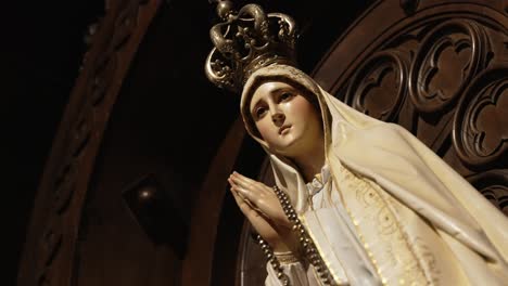 close up of crowned virgin mary statue holding rosary in dim sacred light