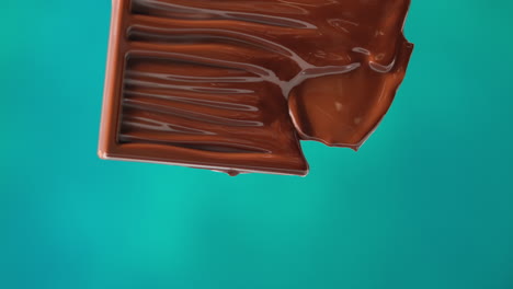 primer plano de una barra de chocolate derretida contra un fondo de color azul con espacio para copiar
