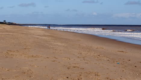 Waves-rolling-onto-Skegness-sandy-beach-with-dog-walkers-on-the-horizon