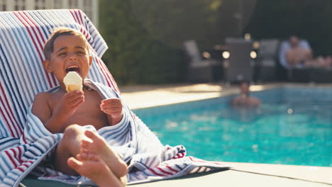 portrait of boy on summer holiday on lounger by swimming pool eating ice cream