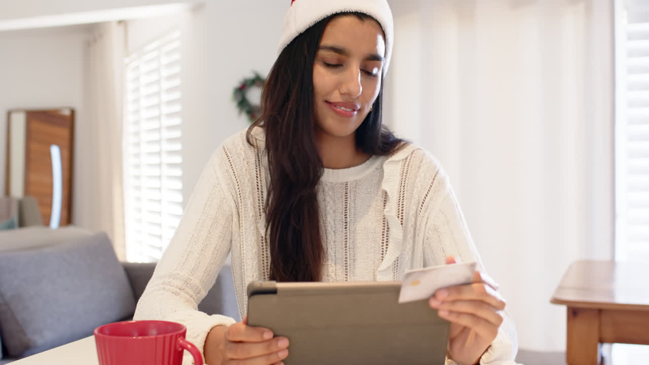 Indian woman in Santa hat shopping online with tablet and credit card