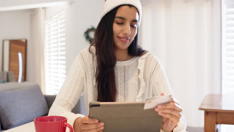 indian woman in santa hat shopping online with tablet and credit card