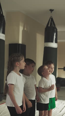 entrenador de artes marciales enseña a los niños en el gimnasio. niño pequeño mira el entrenamiento del instructor con el grupo en el club deportivo en cámara lenta. actividad física y autodefensa
