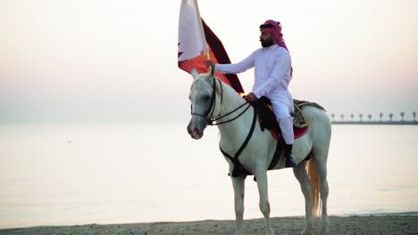 Un-Caballero-A-Caballo-Sosteniendo-La-Bandera-De-Qatar-Cerca-Del-Mar-9