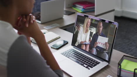 african american woman having a video call with male and female colleagues on laptop at office