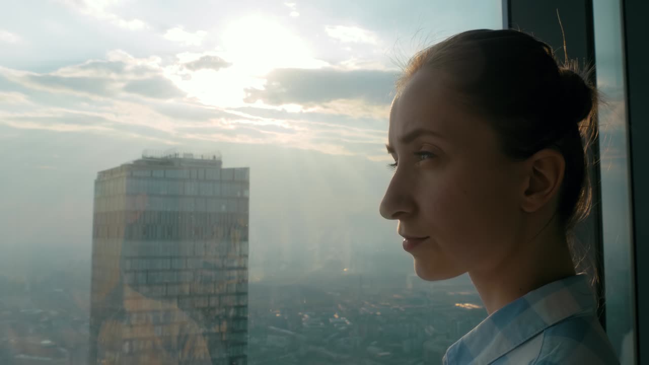 mujer pensativa mirando el paisaje de la ciudad a través de la ventana de un rascacielos - vista lateral