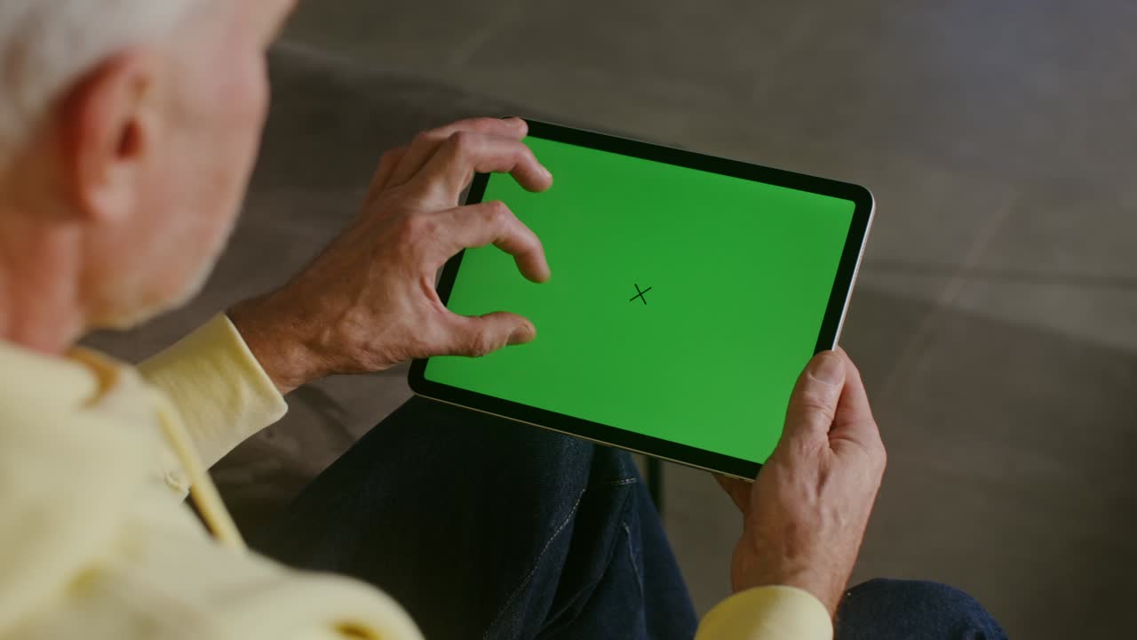 un anciano usa una tableta, desplazando la pantalla con una pantalla verde