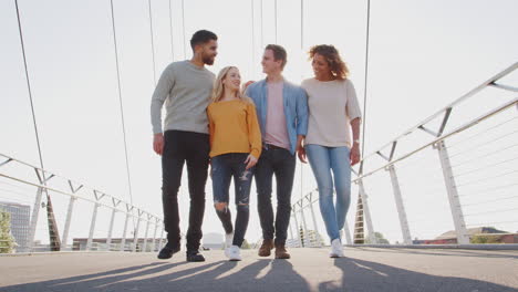 group of young friends walking over city bridge against flaring sun together