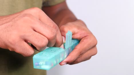 person opening and placing pills into a daily pill organizer