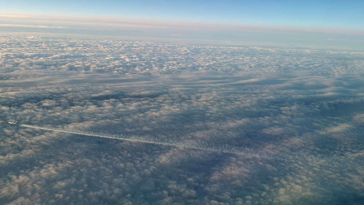 vista increíble desde la cabina de un avión que vuela alto por encima de las nubes dejando un largo rastro de aire de vapor de condensación blanco en el cielo azul