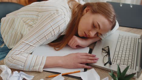 tired woman at home office falling asleep on table with laptop computer crumpled sheets of paper