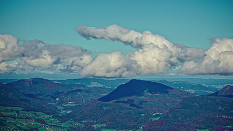 Fluffy-white-clouds-roll-and-curve-in-sky-above-rugged-mountain-peaks-in-countryside