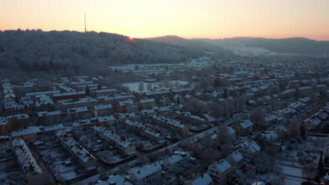 Vista-Aérea-De-Casas-Cubiertas-De-Nieve-De-Winterthur,-Volando-Hacia-El-Sol-Poniente-En-Un-Hermoso-Día-De-Invierno