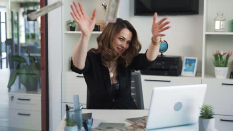 the middle-aged woman is sitting at a desk in an office, in front of her laptop and happily throwing money in front of her