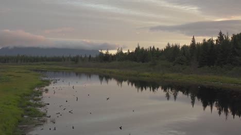 Slow-cinematic-aerial-over-reflective-calm-river-sunrise-over-mountain-wilderness