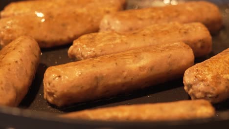 close up of meat alternative sausages cooking gently in frying pan