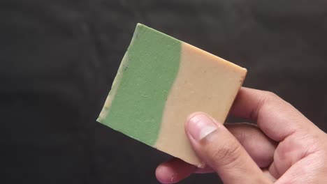 handheld view of a bar of handmade soap with green and beige colors