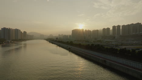 Paisaje-Urbano-Aéreo-De-Hong-Kong-Al-Atardecer-Del-Edificio-De-Rascacielos-Con-Río,-Dron-De-Asia-China-Vuela-Sobre-El-área-Metropolitana-Principal