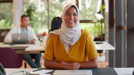 Portrait-Of-Mature-Businesswoman-Wearing-Headscarf-Working-On-Laptop-At-Desk-In-Office